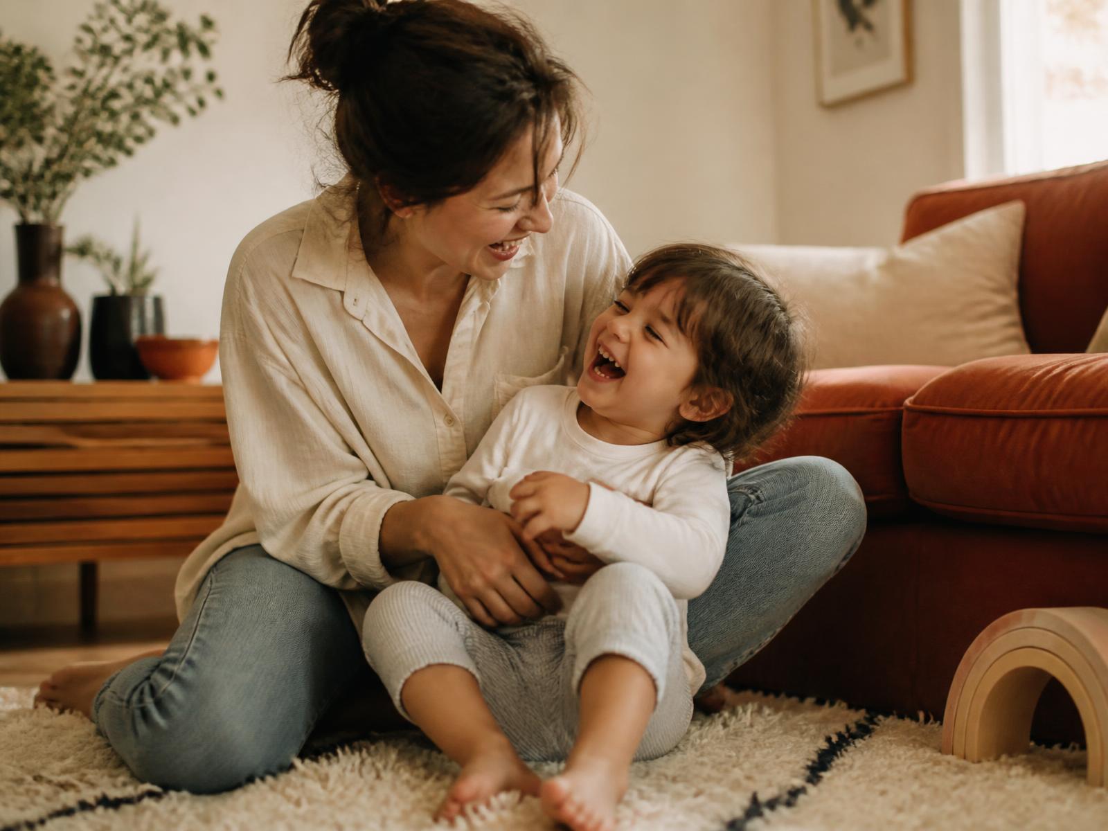 A mother and child laughing together on a rug in a bright room